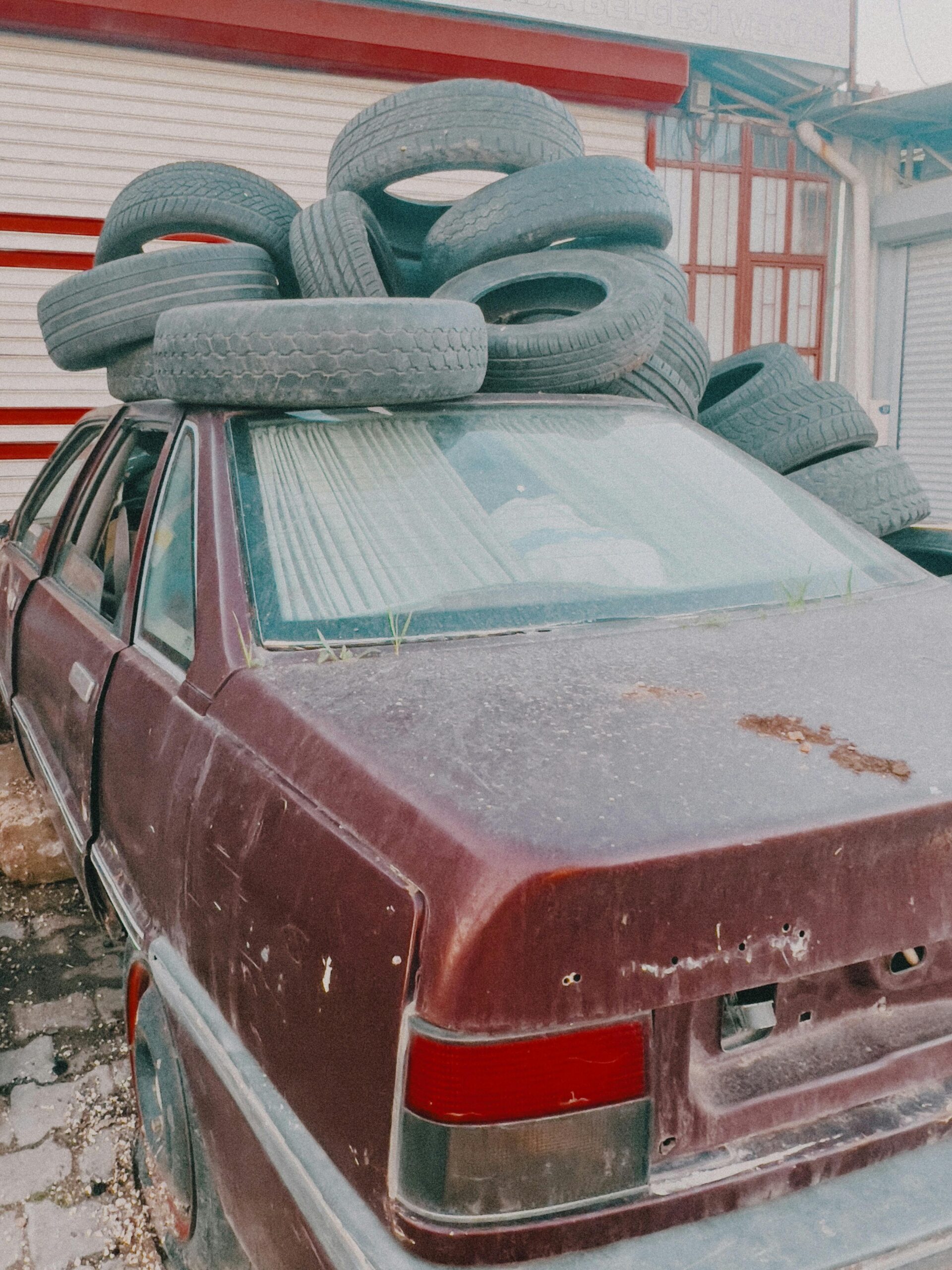 Dusty old car with stacked used tires in urban alley.
