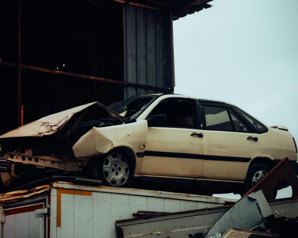 A damaged car sits atop a metal scrap heap, showing a scene of automotive decay.