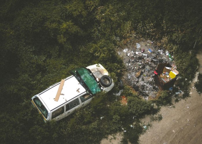 Overhead view of a damaged car and trash in a forested area indicating pollution and neglect.